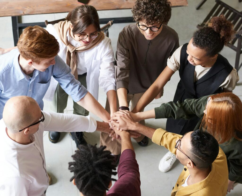 A diverse group of professionals joins hands in a team-building exercise indoors.
