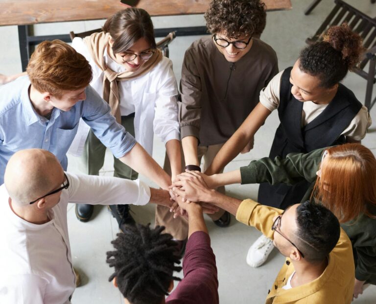 A diverse group of professionals joins hands in a team-building exercise indoors.