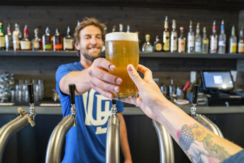 Friendly bartender handing a pint in a lively pub setting.